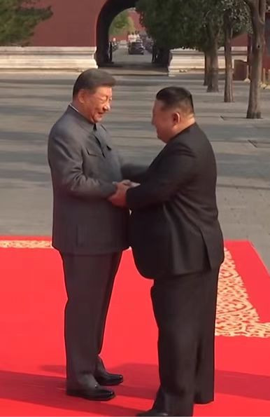习主席同出席纪念大会的金正恩同志握手，欢迎他的来到！